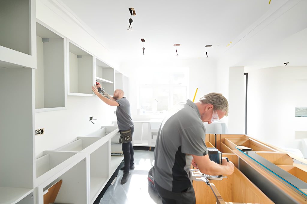 Countertops West Palm Beach installation in progress with workers fitting cabinetry in sunlit modern kitchen space.
