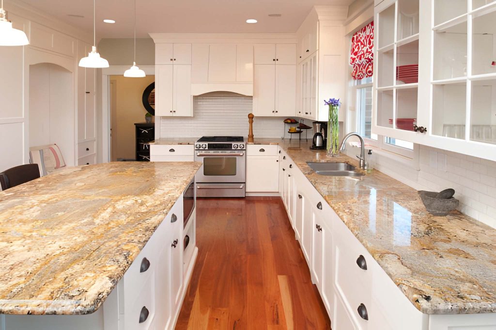 Granite countertops Fort Pierce featured in elegant U-shaped kitchen with island, pendant lighting, and hardwood floors.