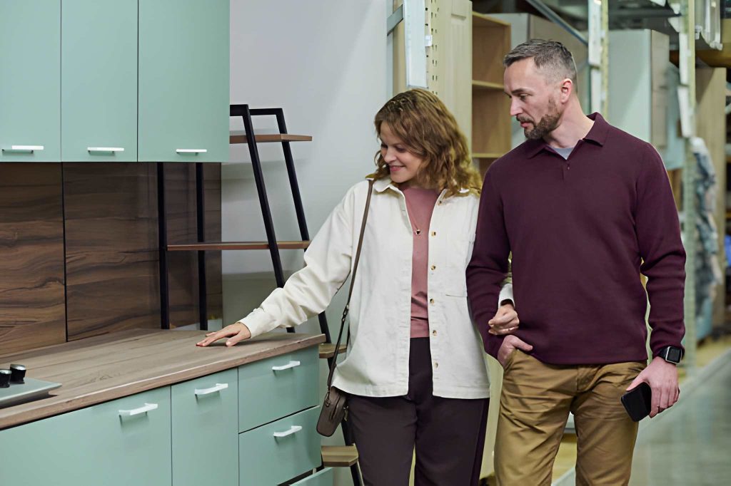 Kitchen cabinets Stuart FL showroom display with customers evaluating mint green cabinetry and wood-textured backsplash.